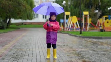 Sonbahar yağmurunda oynayan çocuk. Şemsiyeli çocuk. Her havada çocuklar için açık hava eğlencesi. Çocuklar için su geçirmez giysi, bot ve ceket..