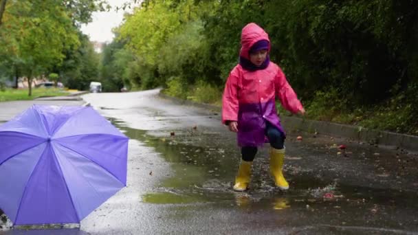 孩子们穿着雨伞和雨靴在外面大雨倾盆地玩耍 孩子在雨中玩耍 小男孩在泥泞的水坑里跳跃 在暴风雨中奔跑的孩子 — 图库视频影像