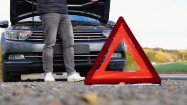 Yol kenarı uyarı üçgeni, bozuk bir araba trafiği uyarısı, yardım çağırmak için cep telefonunu kullanan bir adam. Ulaşım, seyahat kavramı