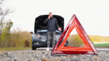 yol tarafında uyarı üçgeni, yardım için arama için cep telefonu kullanan bir adam ile aşağı kırık bir araba gelecek trafik uyarı