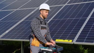 Male engineer in protective helmet installing solar photovoltaic panel system using screwdriver. Electrician mounting blue solar module on roof of modern house. Alternative energy ecological concept.