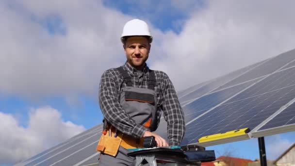 太陽電池ファーム産業の信頼できるエンジニアの肖像画 スタッフの自信をポーズ太陽電池パネルのインストール 太陽電池パネルの近くに立って保護ヘルメットの男性労働者の肖像画を閉じます — ストック動画