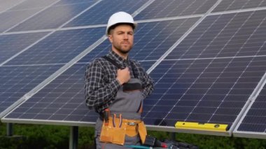 Güneş pili tarım endüstrisinin kendinden emin mühendisinin portresi. Güneş panelinin yanında duran koruyucu kasklı erkek işçinin portresini kapat..