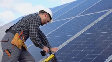 Male engineer in protective helmet installing solar photovoltaic panel system using screwdriver. Alternative energy ecological concept.