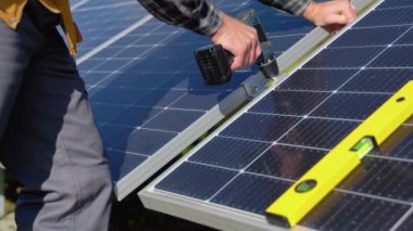 Male engineer in protective helmet installing solar photovoltaic panel system using screwdriver. Alternative energy ecological concept.