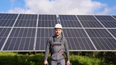 Kasklı erkek mühendis kameraya doğru geliyor ve gülümsüyor.