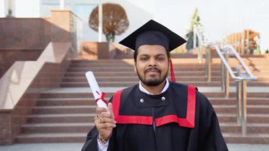 Mutlu mezun. Mezuniyet cüppeli mutlu Hintli adam diplomasını elinde tutuyor..