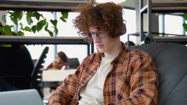 Молодий Рудий Чоловік Навушниками Тримає Ноутбук Чаті Сидячи Зручному Якому — стокове відео