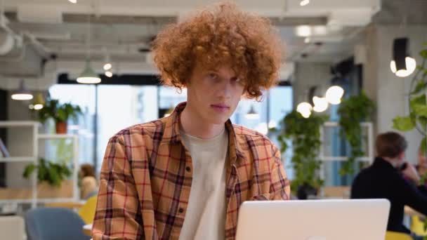 一个穿着光学眼镜的快乐男性自由职业者的画像 他在网上工作时对着相机微笑 坐在咖啡店里 拿着模拟笔记本电脑 — 图库视频影像