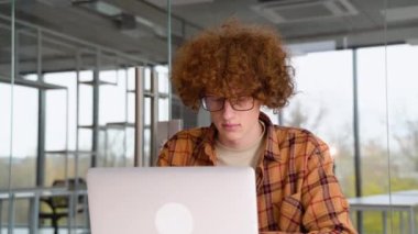 Genç programcı ofiste bir masada oturuyor ve bir dizüstü bilgisayar üzerinde çalışıyor, sarı gömlek giyiyor, blogu için yeni içerikler yaratıyor, serbest çalışan birinin çalışmalarından hoşlanıyor..