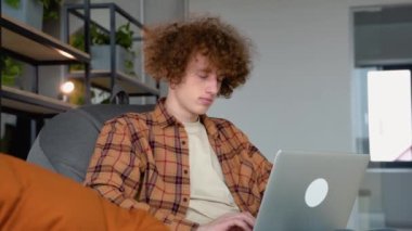 Dizüstü bilgisayarı kullanan genç kızıl saçlı adam iş yerindeki iş yerindeki müşterilerle görüntülü görüşme yapıyor..
