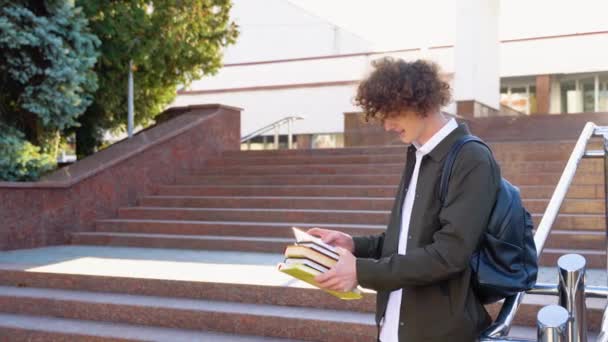 Молодой Рыжеволосый Кудрявый Студент Обнимает Книги Позируя Рюкзаком Возле Здания — стоковое видео