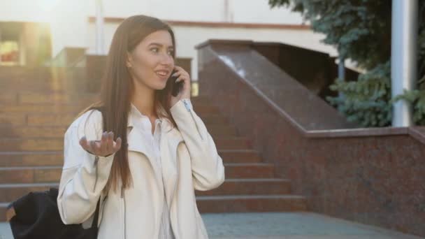 陽気な学生の女の子の本の大学の建物の屋外の近くのバックパックで 携帯電話で話してポーズを抱擁 留学の考え方 — ストック動画