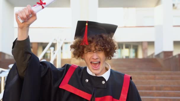 赤髪巻き男とブレーススタンドでマスターマントルと凱旋彼の頭の上に卒業証書を上げる — ストック動画