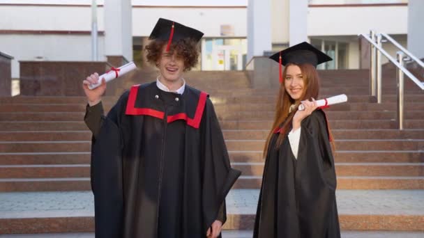 魔法の男と女の子の卒業生は彼らの手に外交官と太陽の光の中で簡単かつ楽しく立っている — ストック動画