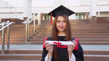 Bir üniversite mezunu yüksek lisans kürsüsünde durur ve önünde diplomasını tutar.