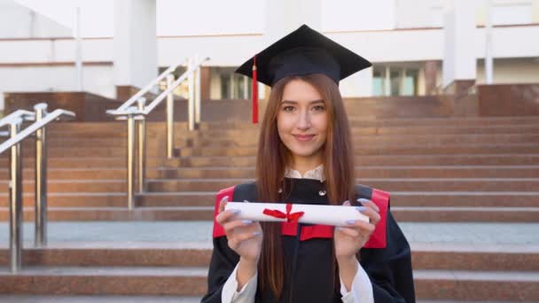 一个大学毕业生站在一个硕士的衣橱里 在她面前拿着一个文凭 — 图库视频影像