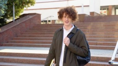Gözlüklü, siyah sırt çantalı, basamaklarda duran ve gülümseyen yakışıklı ve başarılı öğrenci, üniversitenin yakınındaki caddenin dışındaki çerçeveye bakıyor.