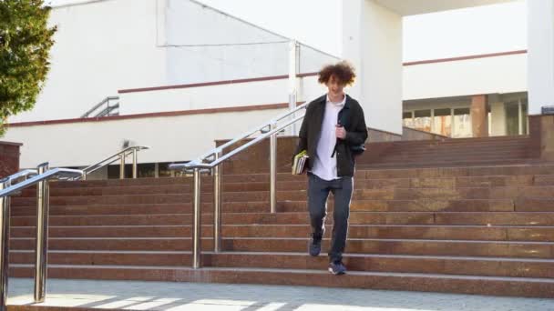 大学やオフィスビルの近くの階段を歩いているハンサムな若い男の学生 所蔵本 — ストック動画
