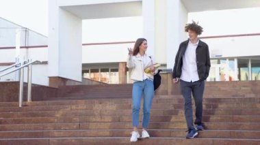 İki şık öğrenci kampüsün etrafında yürüyüp gülümsüyor. Dost canlısı beyaz bir erkek ve kız üniversitenin yakınında birlikte yürüyorlar..