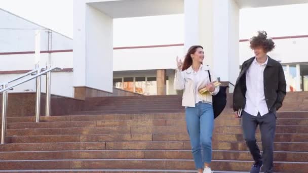 两个时髦的学生走到校园附近笑着 一个友善的高加索男人和一个女孩在大学附近散步 — 图库视频影像