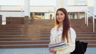 Young girl student smiling near university. Cute girl student holds folders and notebooks in hands. Learning, education concept