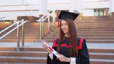 Genç bayan uzman üstadın pelerininde duruyor ve diplomasını zarif bir şekilde tutuyor..