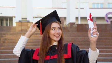 Bir üniversite mezunu elinde diplomasıyla usta bir şapkayla üstat koltuğunda durur.