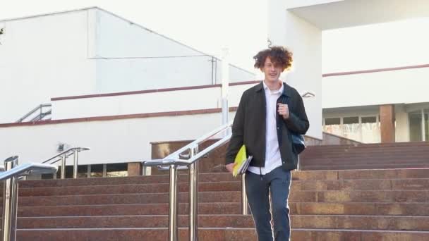 英俊的年轻学生走在靠近大学或办公大楼的楼梯上 拿着书室外 — 图库视频影像