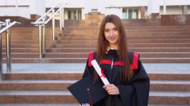 Öğrenim başarısından memnun bir üniversite mezunu açık havada elinde yüksek lisans şapkası ve diplomasıyla duruyor..