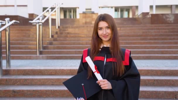 彼女の手の中に修士の帽子と卒業証書と屋外に立つ大学の大学院での研究での彼の成功に満足して幸せ — ストック動画