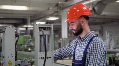 Güvenlik üniforması giyen ve başlık takan profesyonel ağır iş mühendisi bilgisayar kullanıyor. Metal inşaat imalatında gülümseyen bir endüstriyel uzman