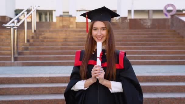 彼女の成功に満足して大学の女性大学院生を訓練するマスターマントルに立っており 彼の手の中に卒業証書を保持している — ストック動画