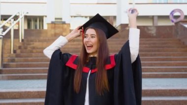 Master MantIe 'den mezun bir üniversite bayan mezunu usta şapkasını tutuyor ve başının üstünde bir diploma sallıyor..