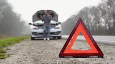 yol tarafında uyarı üçgeni, yardım için arama için cep telefonu kullanan bir adam ile aşağı kırık bir araba gelecek trafik uyarı