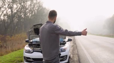 Sisli bir yolda, bozuk bir arabanın yanında bir adam ulaşımı durduruyor..
