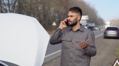Üzgün sürücü araba servisini arıyor, yolda bozuk bir arabanın yanında duran motor arızası var. Araba arızası kavramı.