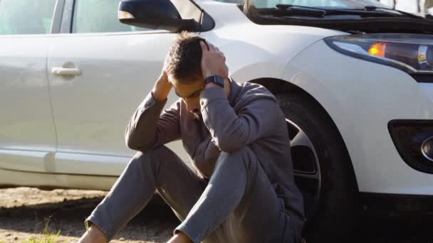 高速道路の真ん中で壊れた車の近くに座っている悲しいドライバ — ストック動画