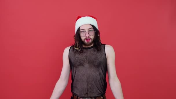 若い笑顔幸せな陽気なゲイの男は 明るい赤の色の背景スタジオの肖像画に隔離メッシュTシャツとクリスマスサンタクロースの赤い帽子を身に着けています ライフスタイル Lgbtq Prideコンセプト — ストック動画