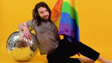 Sarı arka planda, gökkuşağı ve gümüş renkli bayraklı 20 'li yaşlarda beyaz eşcinsel bir adam oturuyor. Insanlar yaşam tarzı lgbtq konsepti