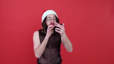 Noel Baba şapkalı genç seksi eşcinsel adam kırmızı arka planda izole edilmiş dudaklar boyuyor. Insanlar yaşam tarzı lgbtq konsepti