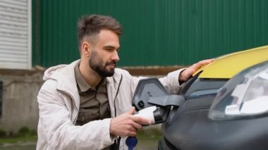 Havalı bir adam elektrikli araca kablo bağlıyor ve pilleri şarj ediyor. Erkek el kargo EV vagonuna güç bağlantısı yerleştirir