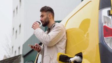 Bir adam elektrikli araba şarj ederken kahve içer..