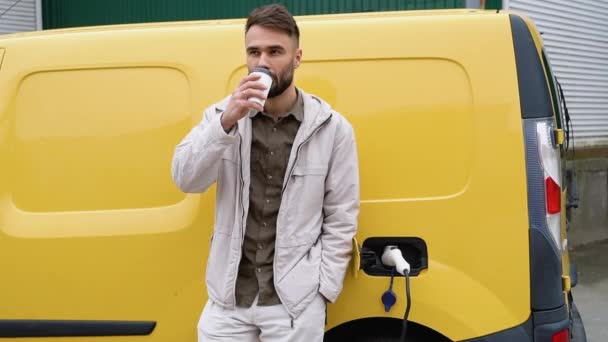 Uomo Beve Caffè Appoggiandosi Alla Sua Auto Elettrica Carico Piedi — Video Stock