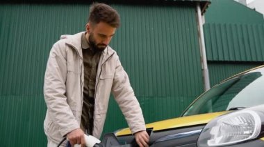 Happy man charges an electric car at a charging station. Electric car charging