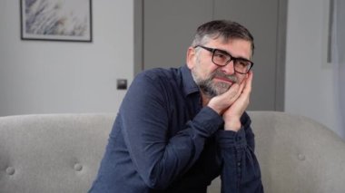 Diş ağrısı ya da diş hastalığından dolayı evde kıdemli yakışıklı bir adam elleriyle ağzına dokunuyor.