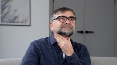 Boğazında korkunç bir ağrı var. Evdeki kanepede oturan sinirli adam boynuna dokunuyor.