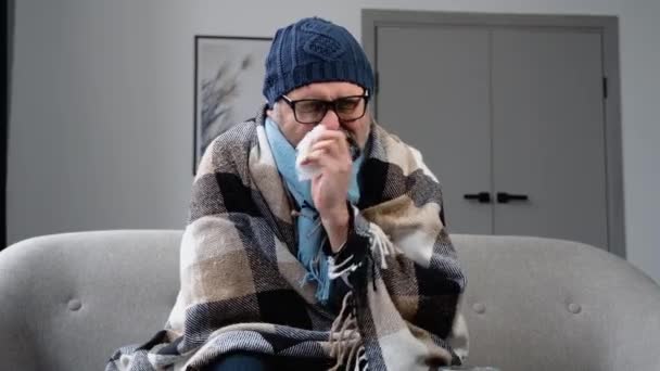 病気の冷凍老人はソファに座って 帽子をかぶる組織が鼻水を吹いている熱を得た 風邪を引く 近くの薬のヒープ — ストック動画