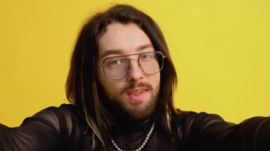 Genç eşcinsel adam sarı arka planda selfie çekiyor.