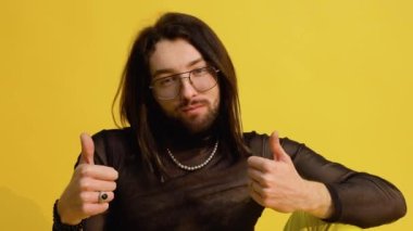 Gülümseyen mutlu biseksüel adam gözlüklü ve örgü tişörtlü sarı arka planda..